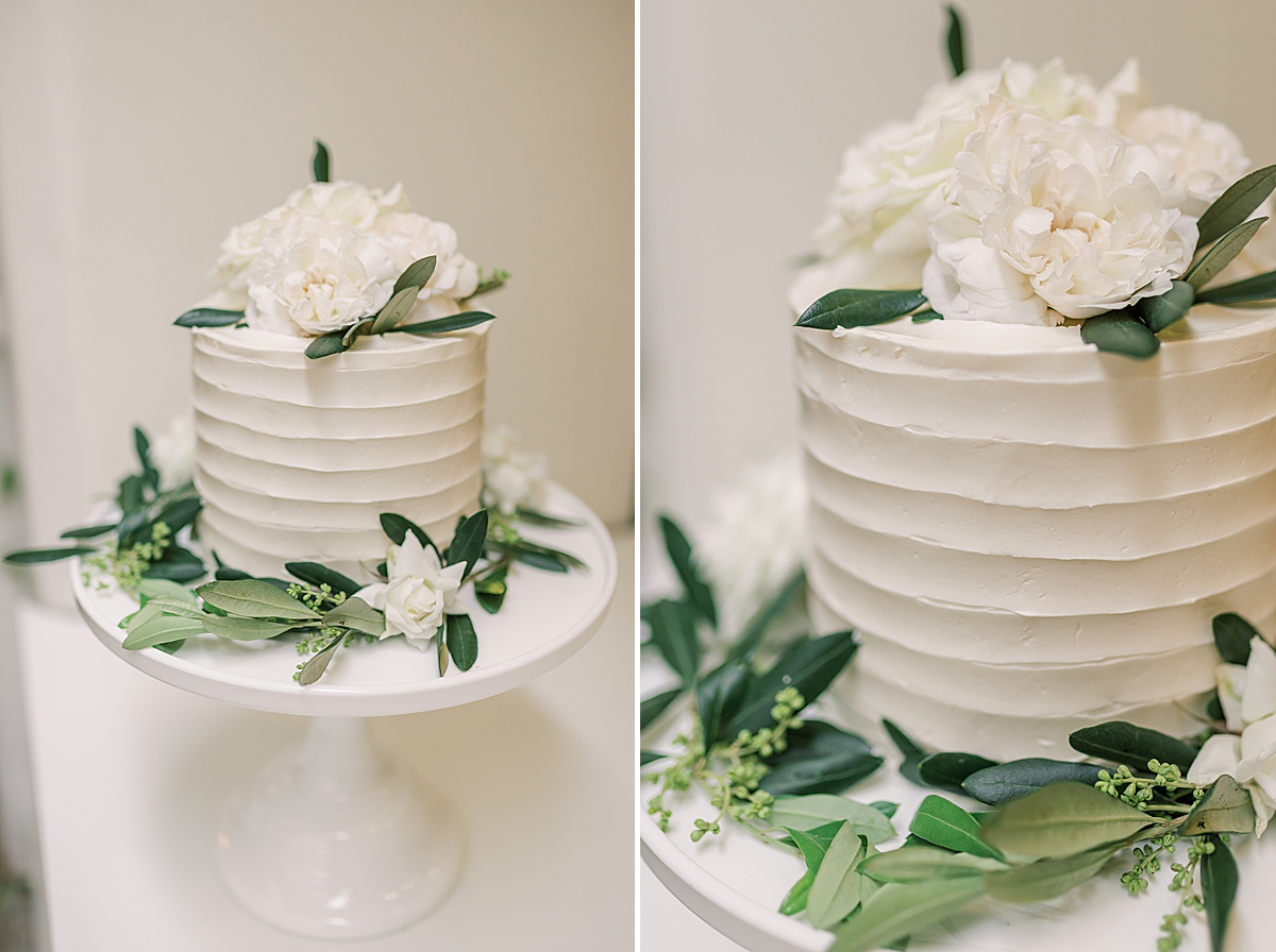 The bride and groom's wedding cake with green eucalyptus leaves surrounding the platter and garnished with white roses on its top.