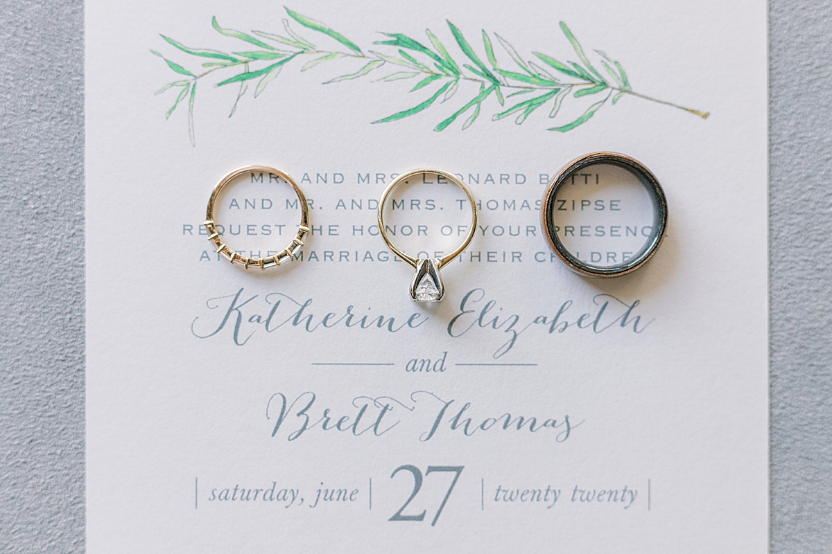 The couple's wedding bands with the bride's engagement ring on their wedding invitation.