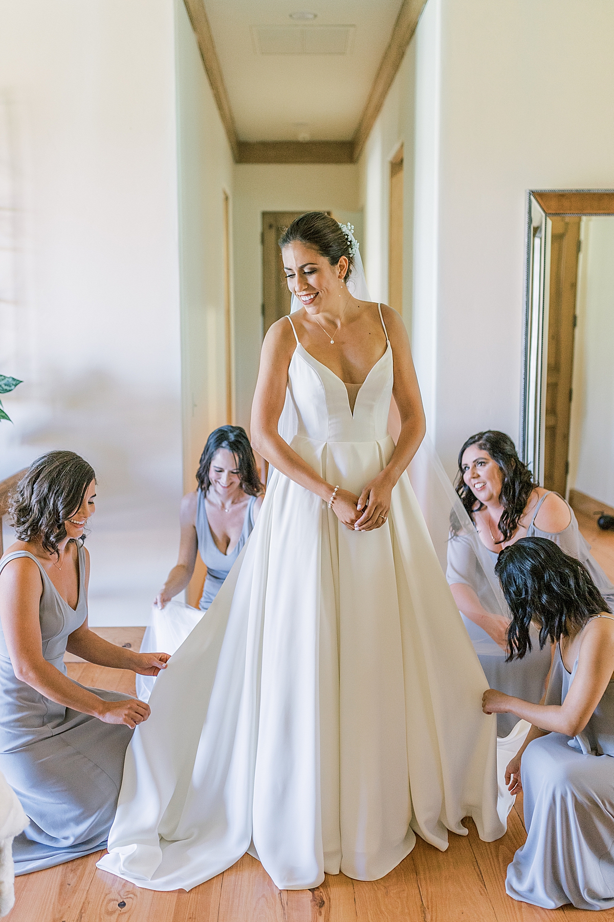 Kat's bridesmaids helping fluff her dress before finishing getting ready.