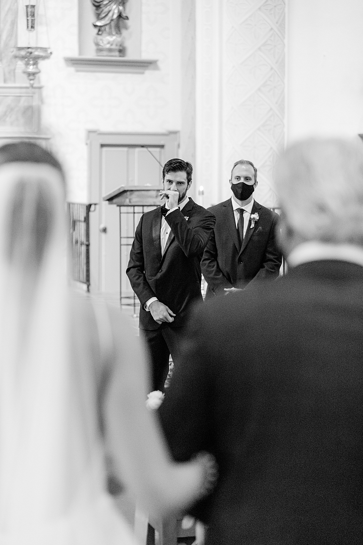 The groom raising his hand to his mouth in awe of his bride as she walks down the aisle towards the altar during their San Luis Obispo Mission wedding.