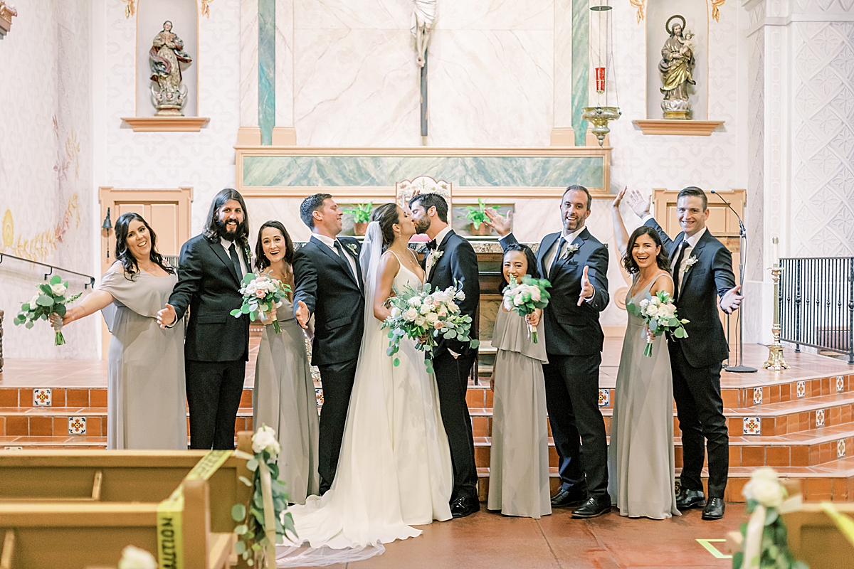 The couple sharing a kiss as their bridal party cheers them on during their San Luis Obispo Mission wedding.