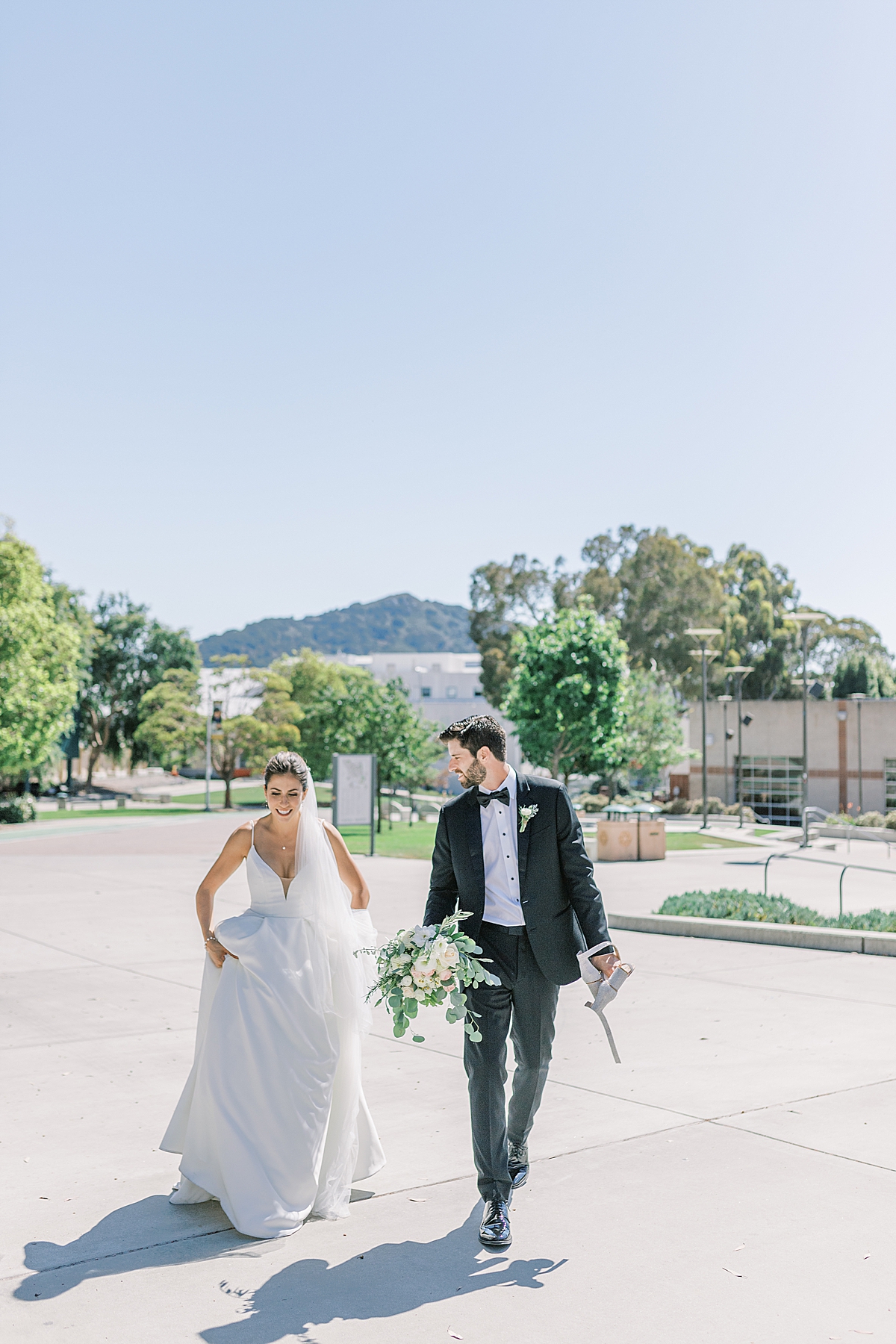 The newlyweds walking through their old college campus in their wedding attire on their San Luis Obispo Mission wedding day.