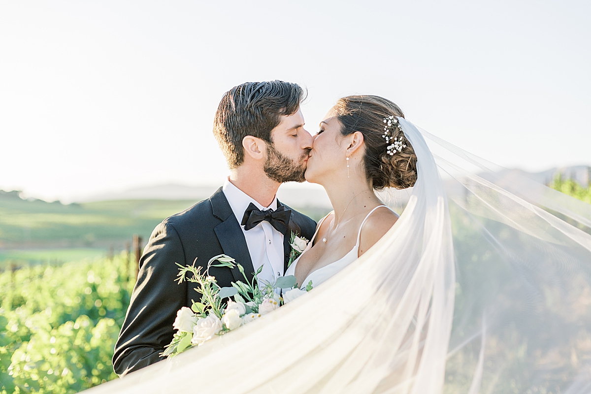 The couple sharing a kiss as the bride's veil wraps around their bodies and heads towards the camera.