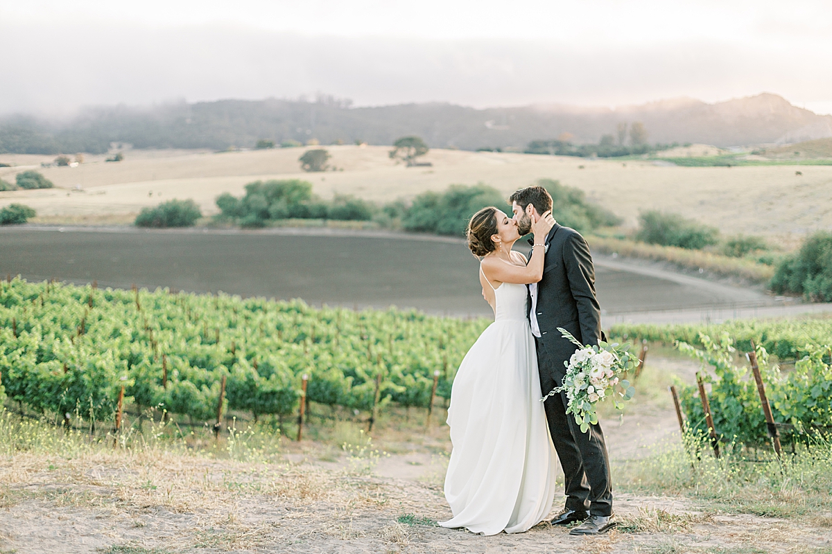 The couple sharing a kiss as the last bit of sunlight disappears behind the mountains surrounding their San Luis Obispo Mission Wedding venue.