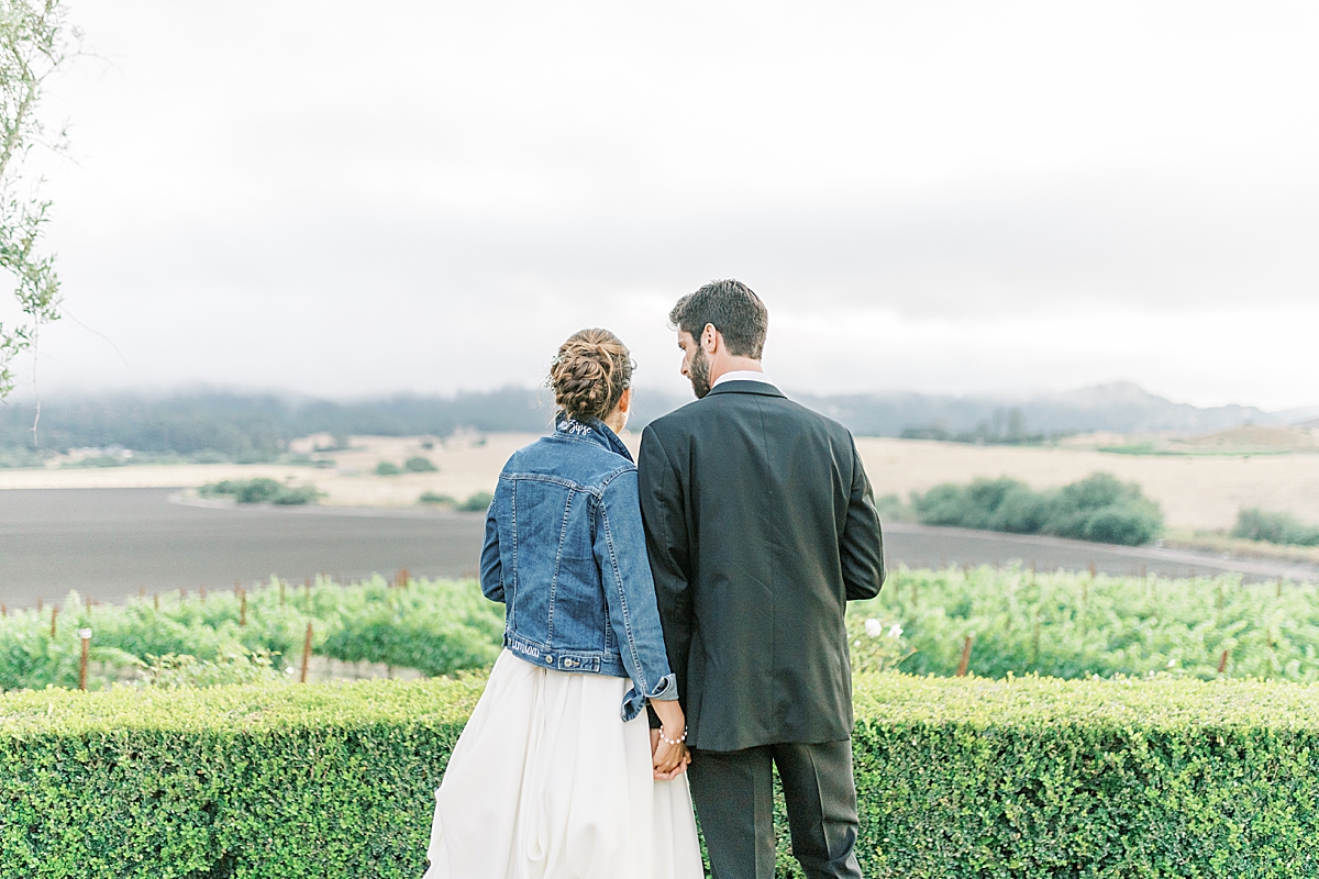 Kat & Brett looking across the vineyard together while holding hands at their San Luis Obispo Mission wedding.