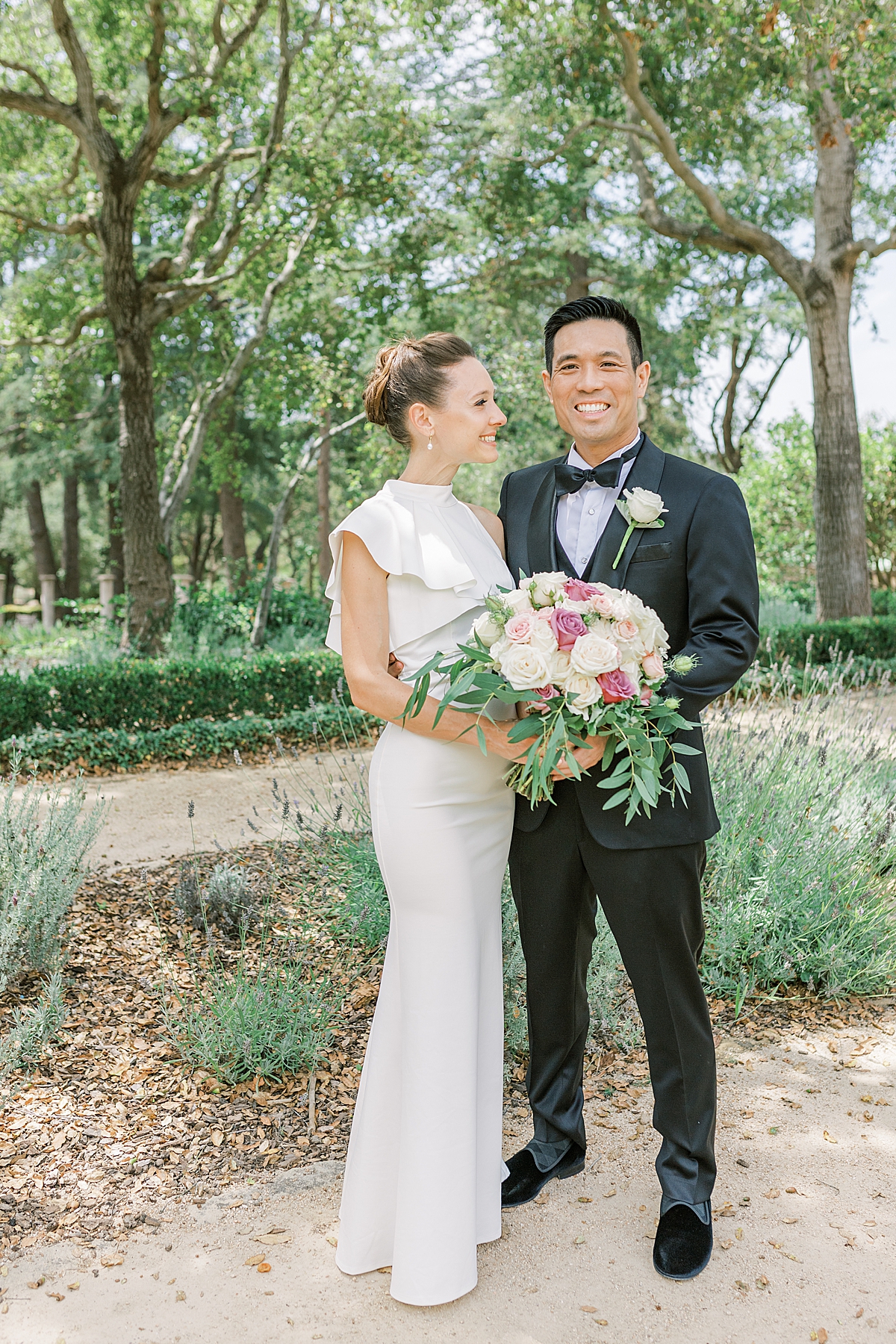 Erica is smiling at Gideon and Gideon is looking at the camera as they hold her bouquet of flowers between them just minutes before they traveled to the ceremony space of their Montecito Church Wedding.