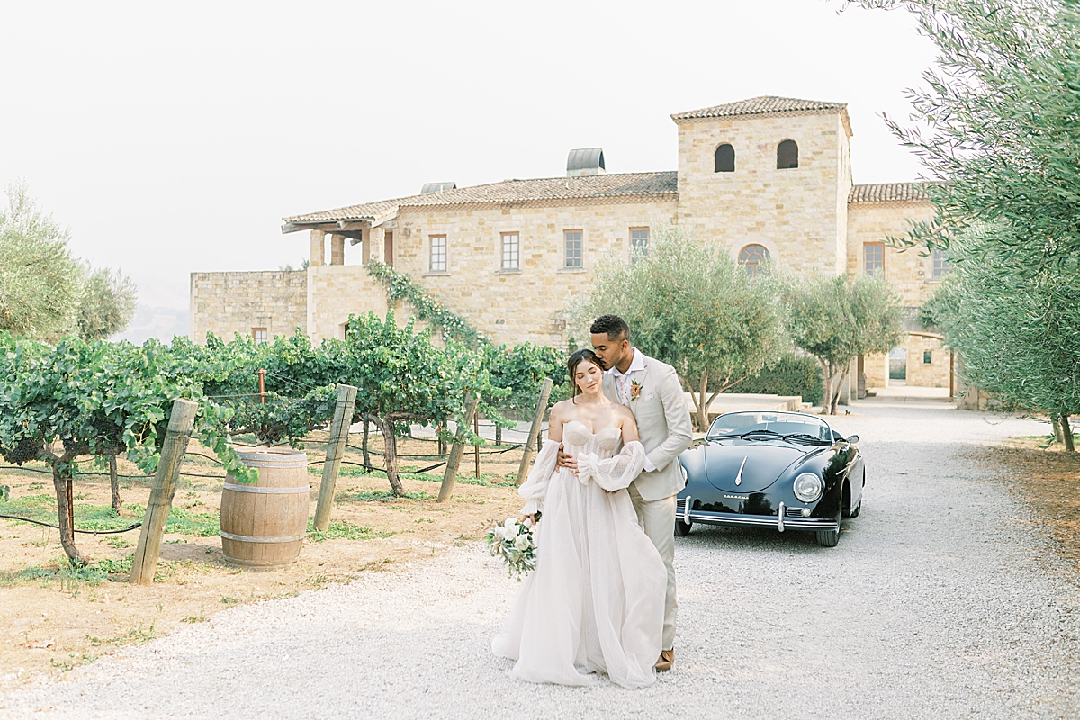 The couple standing in front of the vintage car and holding each other close at this Sunstone Villa Wedding editorial.