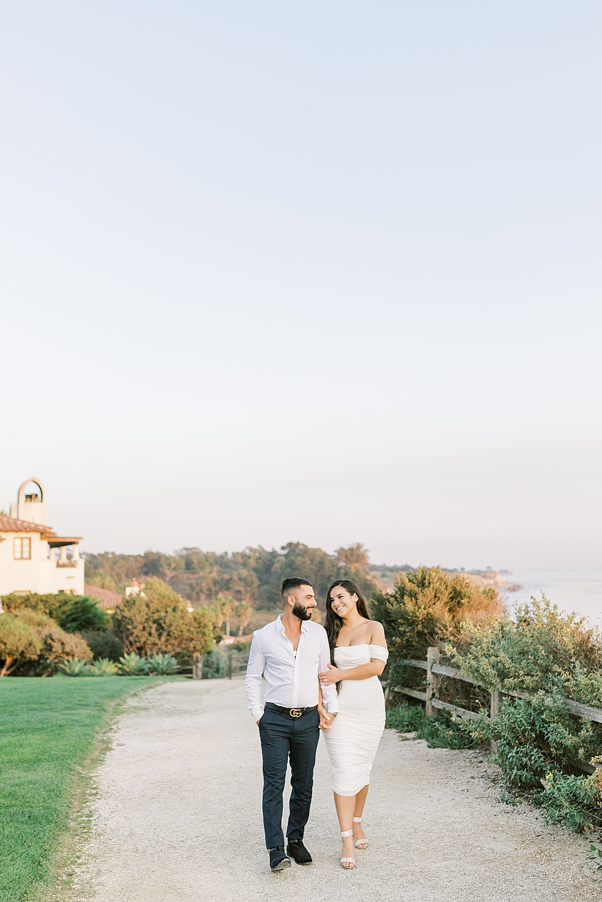 The couple smiling at each other as they walk down a pathway holding hands during their Santa Barbara Elopement at the Ritz-Carlton Bacara in California. 