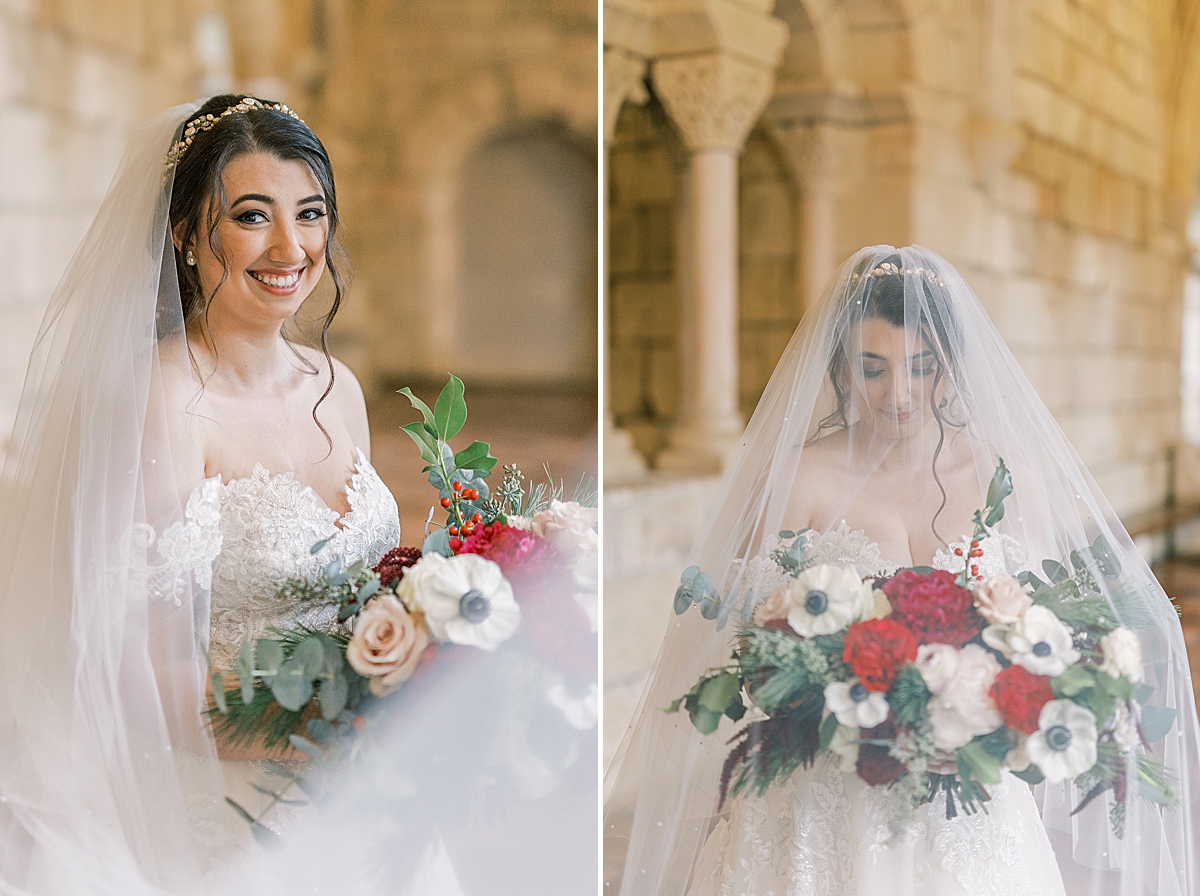 The bride smiling at the camera while wearing her veil over her face and holding her bouquet. 