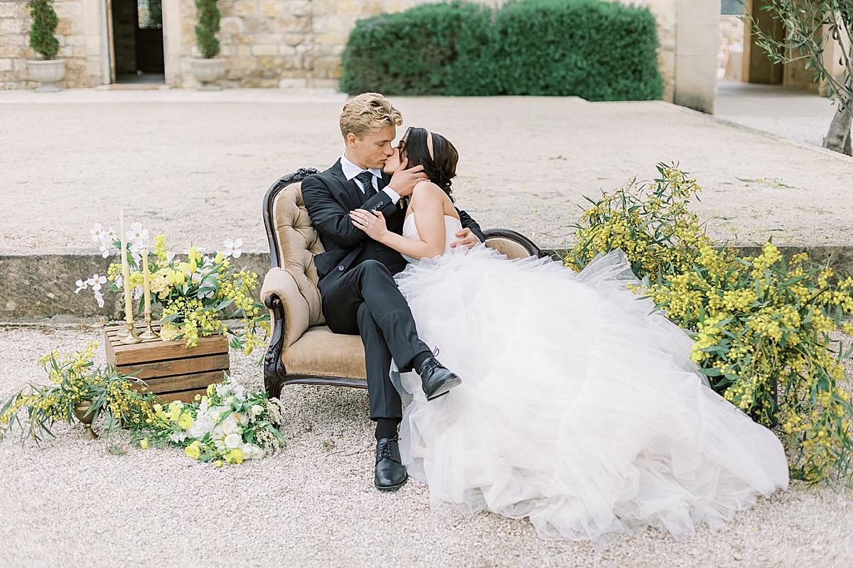 Kendall & Miller sharing a kiss on a love seat in front of the Sunstone Villa at their at the couple's Yellow & Black Micro-Wedding
