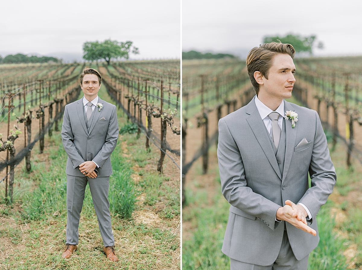 The groom wearing a gray suit and smiling at the camera while standing in the vineyards.