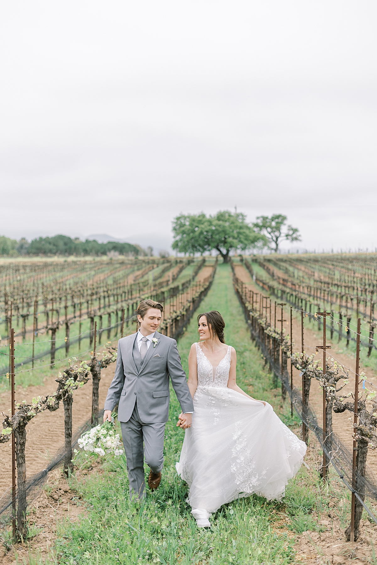 The couple holding hands while walking through the vineyard at their Southern California Winery Wedding at Sunstone Villa in Santa Ynez, California.