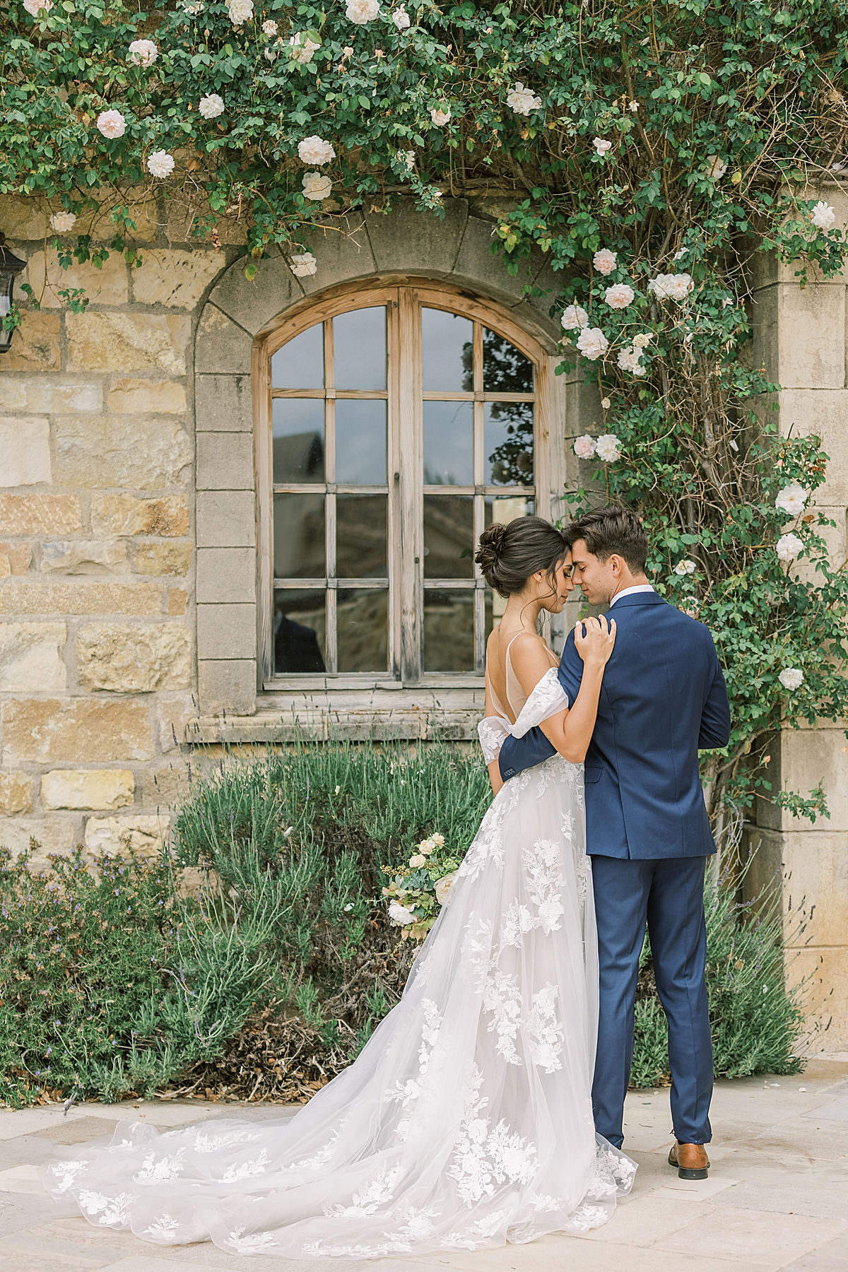A bride and groom under a crawling vine decorated with white roses.